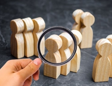 Hand holding a magnifying glass looking at figurines of people